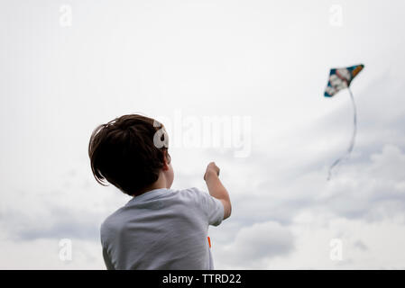 Rear view of boy flying kite in cloudy sky Stock Photo