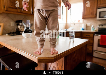 Low section of boy standing on wooden table in kitchen
