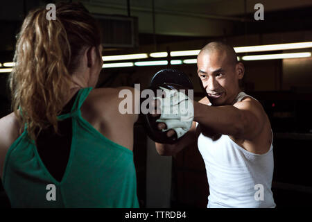 Smiling trainer assisting female boxer in boxing ring at gym Stock Photo