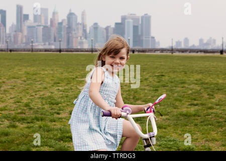 Portrait of happy girl riding bicycle with skyline in background Stock Photo