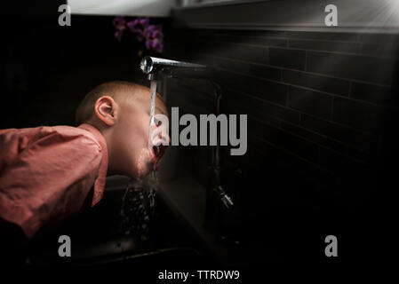 Side view of boy drinking water from faucet in kitchen at home Stock Photo