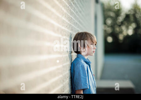 Thoughtful boy looking away while leaning against wall Stock Photo