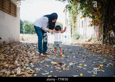 Mother assisting son in walking on street Stock Photo