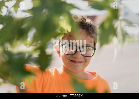 Portrait of smiling boy wearing eyeglasses seen through leaves Stock Photo