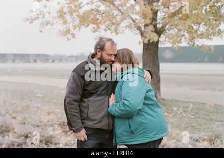 Mature couple wearing warm clothing embracing on field Stock Photo
