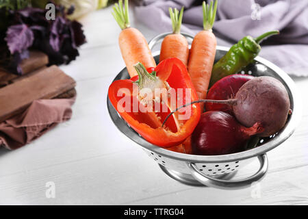 Fresh vegetables in colander on wooden table Stock Photo