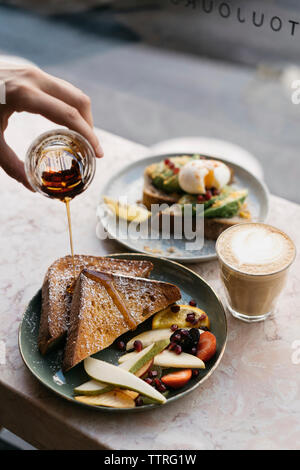 Cropped hand of woman pouring honey on toasted breads in plate at cafe Stock Photo