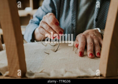 Midsection of upholsterer stitching fabric on chair in workshop Stock Photo