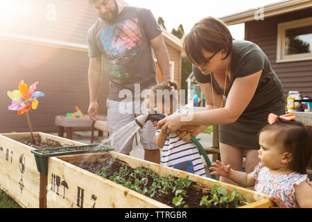 Parents with children watering plants at backyard Stock Photo