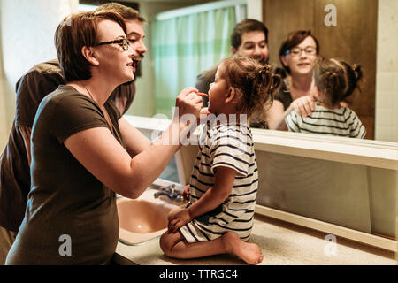 Father standing by mother brushing teeth of daughter in bathroom Stock Photo