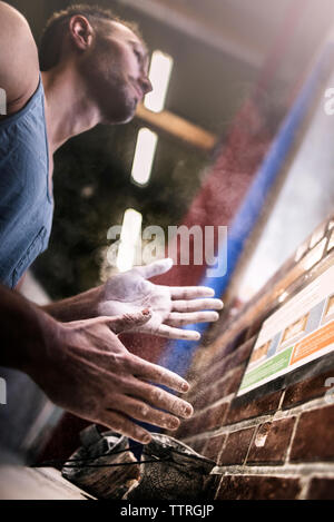 Low angle view of athlete chalking hands while standing in illuminated gym Stock Photo