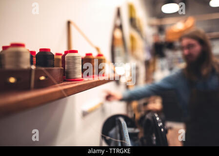Close-up of spools on shelf with shoemaker in background Stock Photo