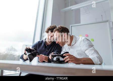 Engineers examining virtual reality simulators at table in office Stock Photo
