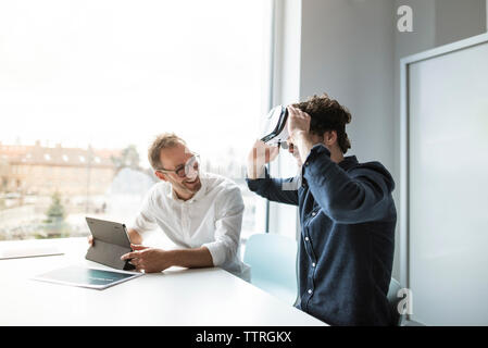 Smiling engineer looking at colleague examining virtual reality simulator in office Stock Photo