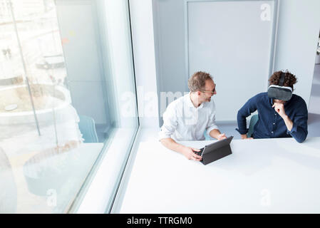 Engineer looking at male colleague examining virtual reality simulator in office Stock Photo