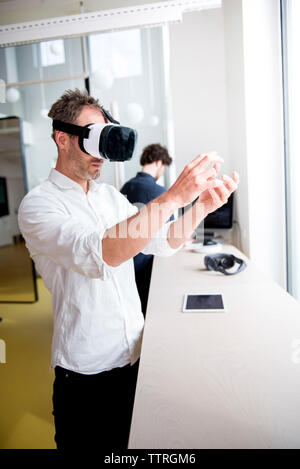 Engineer examining virtual reality simulator while coworker using computer at table Stock Photo