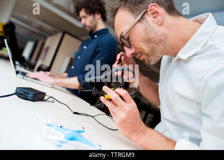 Engineer examining drone while coworker using laptop computer in office Stock Photo