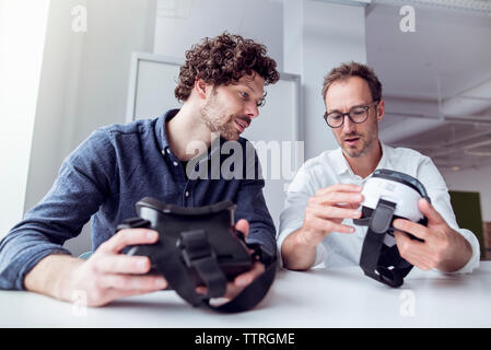 Technicians examining virtual reality simulators while sitting at table in office Stock Photo