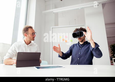 Engineer with tablet computer looking at coworker examining virtual reality simulator in office Stock Photo