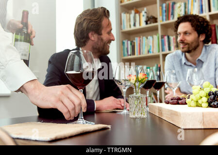 Cropped hands of bartender holding wineglass while friends talking at table in tasting room Stock Photo