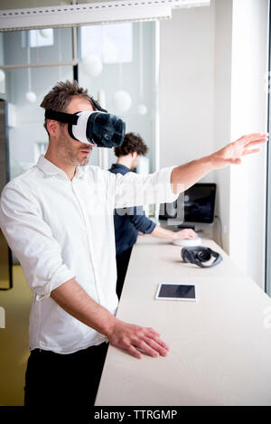 businessman examining virtual reality simulator while coworker using computer in office Stock Photo