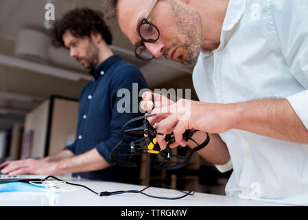 businessman examining drone while coworker using laptop computer in office Stock Photo
