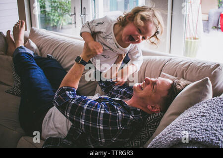 Happy father lifting up daughter while lying on sofa at home Stock Photo