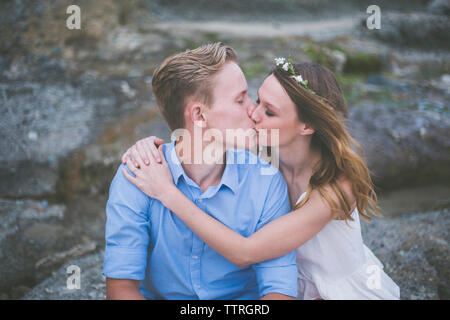 Couple kissing while sitting on rock at beach Stock Photo