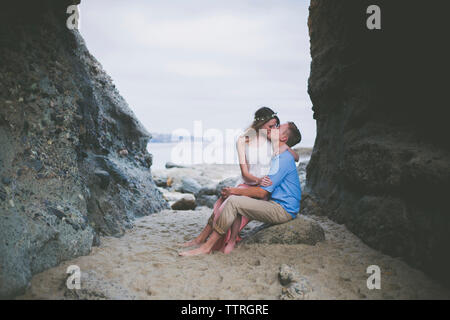 Romantic couple kissing while sitting on rock at beach Stock Photo