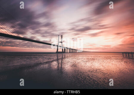 Silhouette Vasco Da Gama Bridge over Tagus River against cloudy sky during sunrise Stock Photo