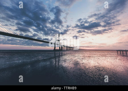Silhouette Vasco Da Gama Bridge over Tagus River against cloudy sky at sunrise Stock Photo