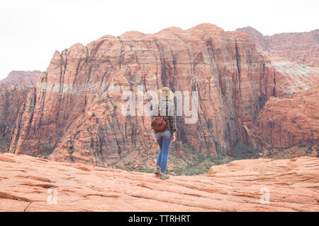 Rear view of woman with backpack looking at mountains while standing on rock formation against sky in Snow Canyon State Park Stock Photo