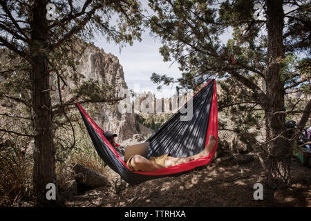 Man using laptop while resting in hammock over field in mountain Stock Photo
