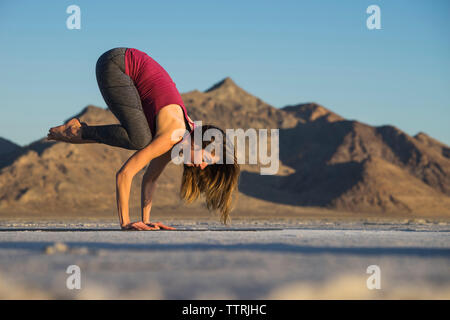 Side view of woman practicing crow pose against clear blue sky during sunset Stock Photo