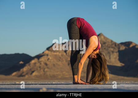 Side view of woman practicing yoga against clear blue sky during sunset Stock Photo