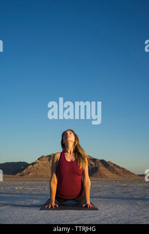 Woman practicing upward facing dog position against clear blue sky during sunset Stock Photo
