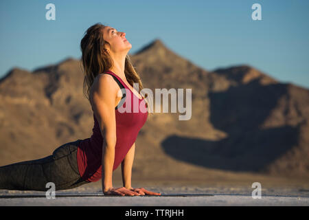 Side view of woman practicing upward facing dog position against clear blue sky during sunset Stock Photo