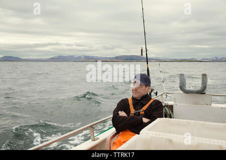 Mature fisherman sitting in fishing boat at sea against cloudy sky Stock Photo