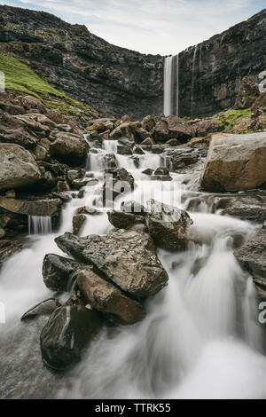 Idyllic view of stream flowing through rocks against waterfall Stock Photo