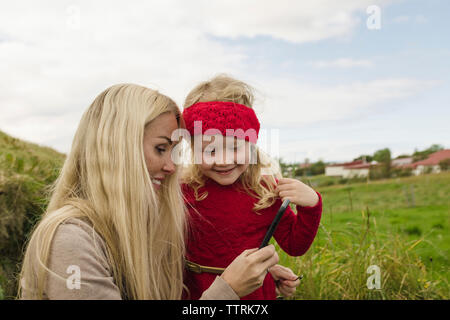 Happy mother and daughter looking at smart phone on field Stock Photo