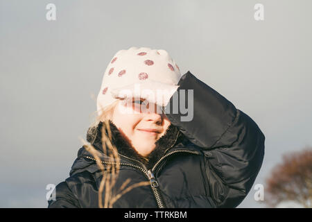 Portrait of cute girl shielding eyes from sunlight while wearing warm clothing Stock Photo