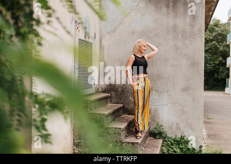 Full length of woman looking away while standing on steps against concrete wall Stock Photo