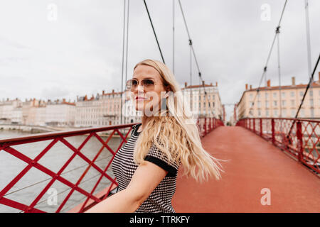 Confident woman wearing sunglasses walking on Paul-Couturier Footbridge over Saone River against buildings in city Stock Photo