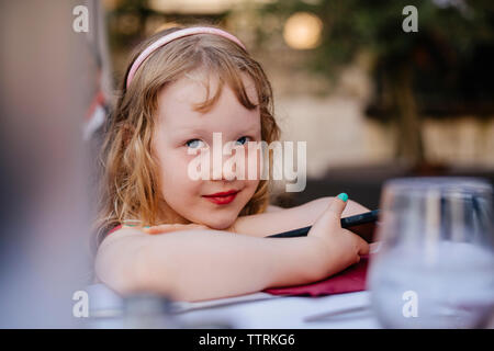 Portrait of cute girl with mobile phone sitting at sidewalk cafe in city Stock Photo