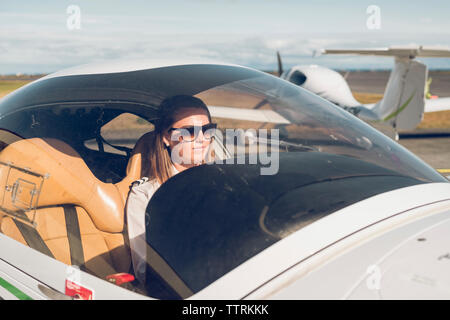 Confident female pilot wearing sunglasses sitting in airplane seen through windshield Stock Photo