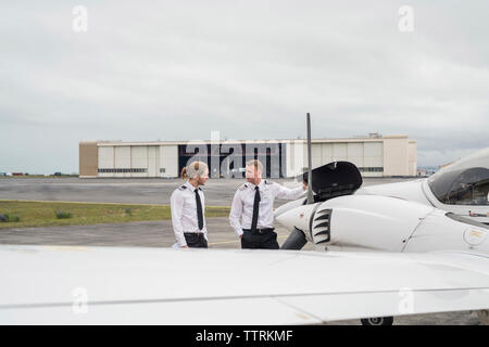 Engineer showing airplane parts to male trainee while standing against cloudy sky on airport runway Stock Photo