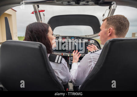 Rear view of male pilot giving training to female trainee while sitting in airplane at airport Stock Photo