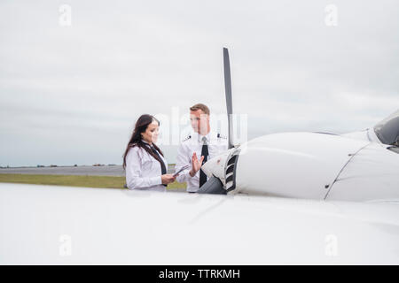 Engineer showing airplane parts to female trainee while standing against cloudy sky on airport runway Stock Photo