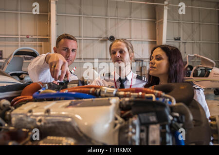 Male engineer showing airplane engine to trainees while standing in hangar Stock Photo