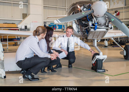 Male engineer showing airplane wheel to trainees while crouching on floor in hangar Stock Photo